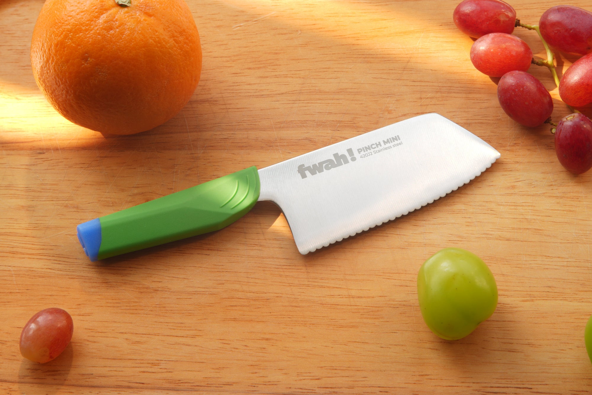 Knife with a green handle on a wooden cutting board with fruits